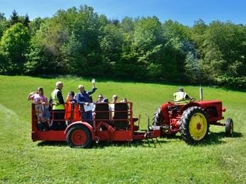 Red tractor in field towing trailer filled with people waving