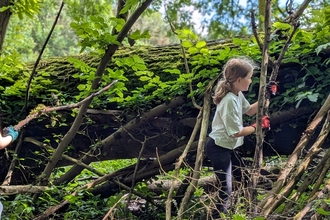 Two girls making a den against a mossy tree