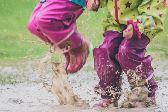 Two young people in wellies jumping in a puddle