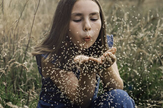 Young person blowing seeds towards the camera