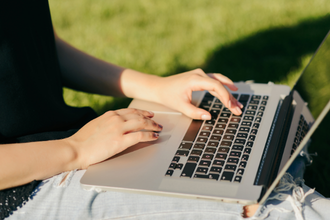 Female individual sat outside typing on a laptop