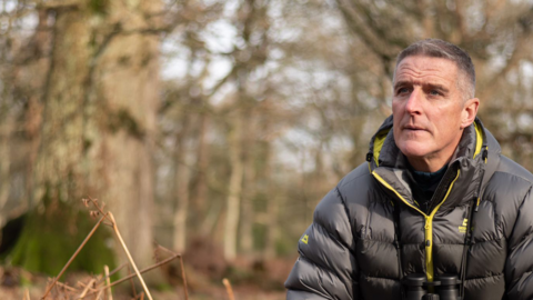 Iolo Williams crouched amongst scrub