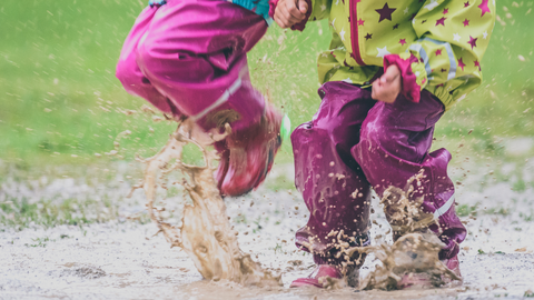 Two young people in wellies jumping in a puddle