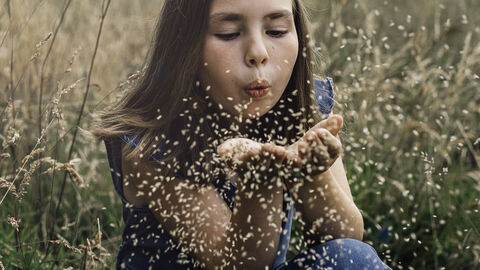 Young person blowing seeds towards the camera