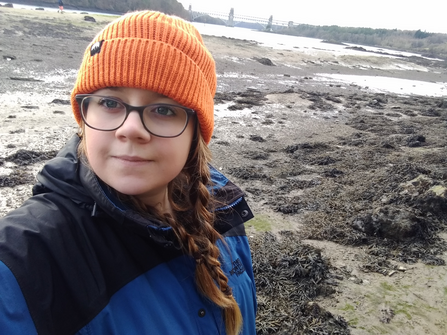 Emma on a muddy shore, smiling at the camera