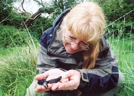 Lady crouched with small, black newt in her hands