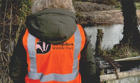 The back of a person with a high vis jacket bearing the Shropshire Wildlife Trust logo