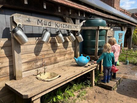 Two children enjoy playing with outdoor mud kitchen